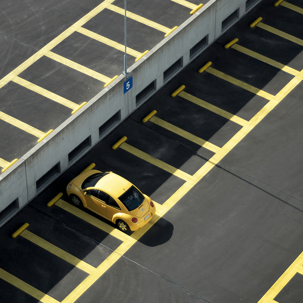 Parking samochodowy z żółtymi liniami oznaczającymi miejsca, na jednym z nich stoi żółty samochód.