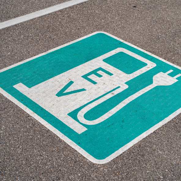 Znak na ulicy przedstawiający stację ładującą dla samochodu elektrycznego na niebieskim tle.