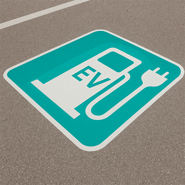 Znak na ulicy przedstawiający stację ładującą dla samochodu elektrycznego na niebieskim tle.