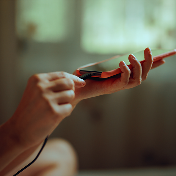 Obraz przedstawia smartphone trzymany w ręku przez kobietę, która podłącza do niego kabel z ładowaniem.