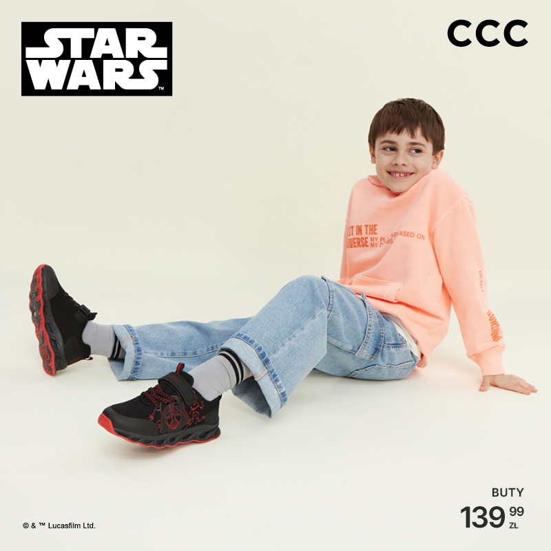 Chłopiec w bluzie i jeansach siedzi, prezentując czarne buty Star Wars z czerwonymi elementami. Logo Star Wars i CCC widoczne.