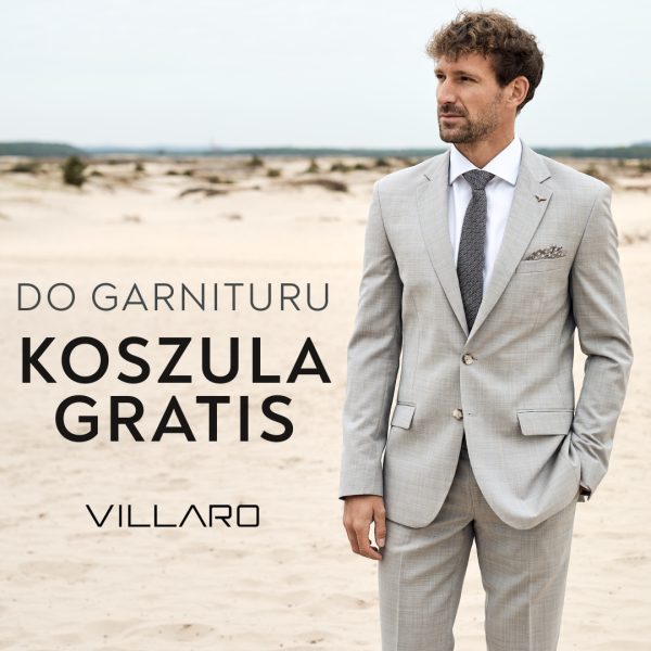 Mężczyzna w jasnoszarym garniturze i krawacie, stojący na piaszczystym terenie, z napisem 'DO GARNITURU KOSZULA GRATIS VILLARO'