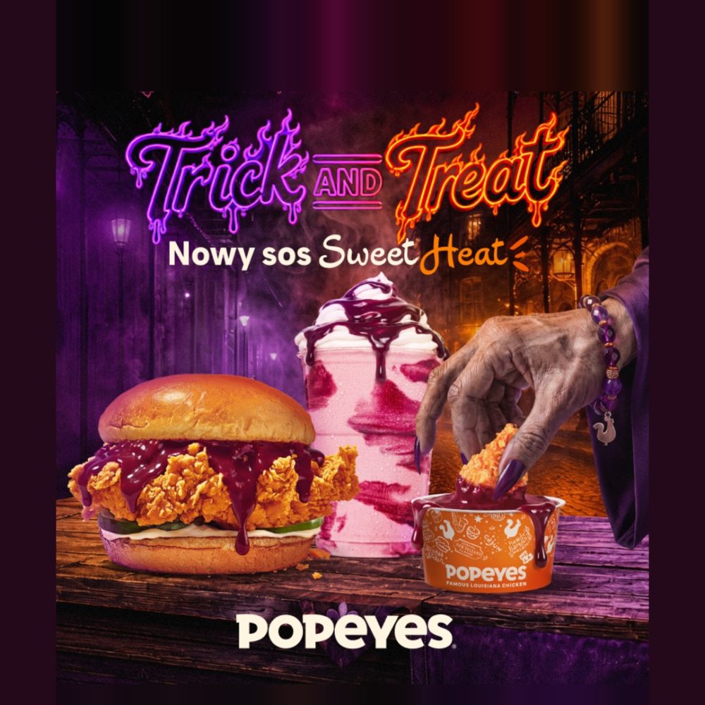 Reklama Popeyes z halloweenową grafiką, przedstawiająca kanapkę z kurczakiem, shake'a i kawałek kurczaka maczany w sosie Sweet Heat przez rękę wiedźmy. Napis "Trick and Treat" i "Nowy sos Sweet Heat".